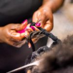 Close-up of a hairstylist hands using tools while braiding and extending customer's hair in her beauty salon